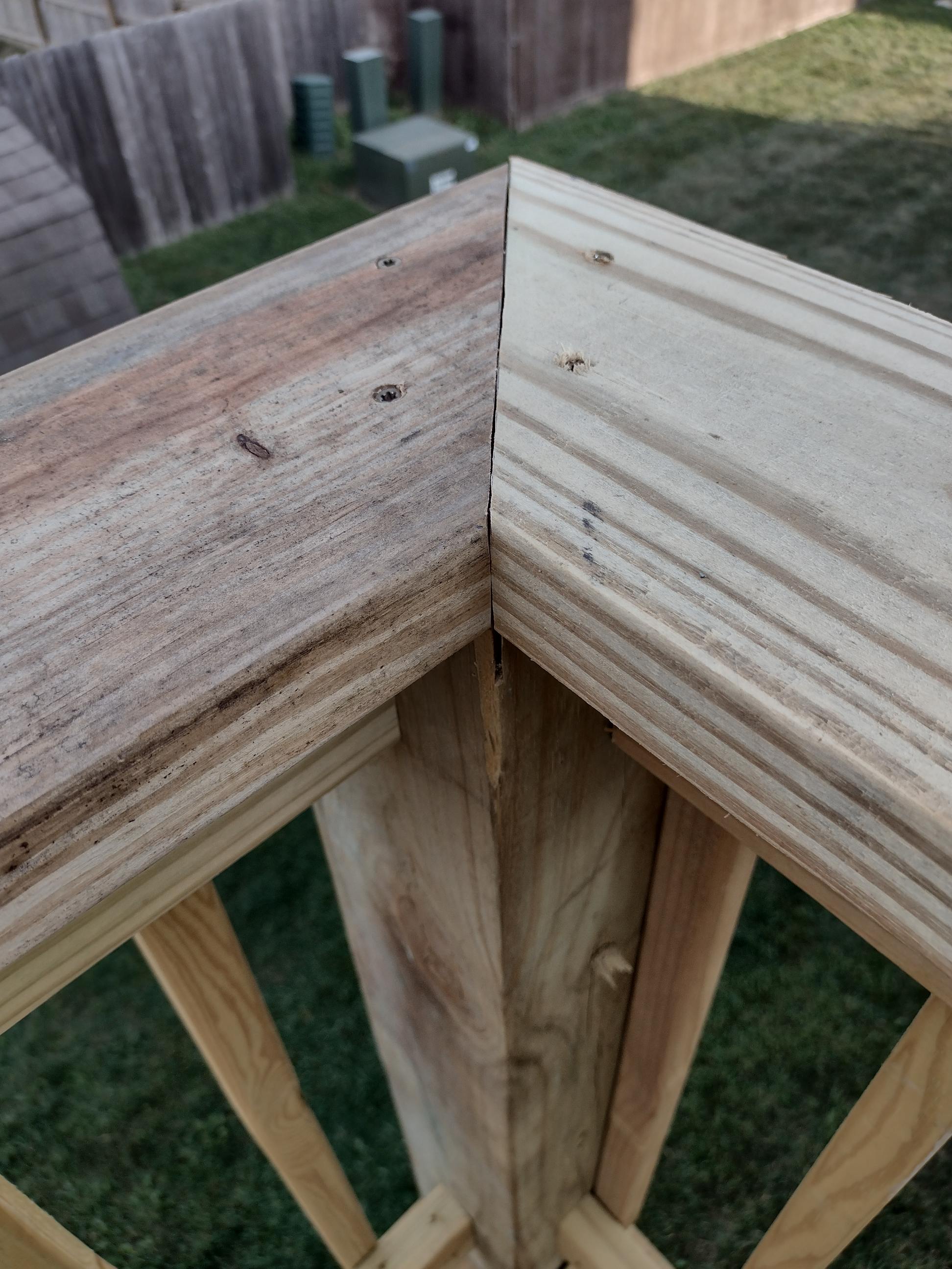 Weathered deck railing corner in Kansas City showing the top rail miter joint opened up as the treated lumber dried and shrank